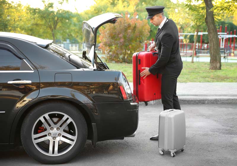 Chauffeur putting suitcase in car trunk